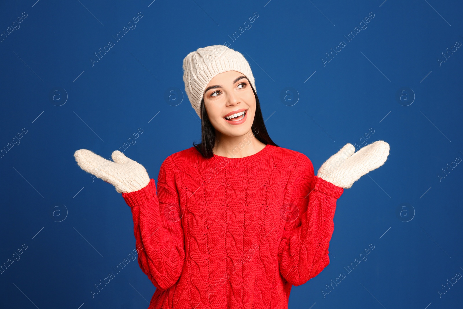 Photo of Young woman wearing warm sweater, mittens and hat on blue background. Winter season