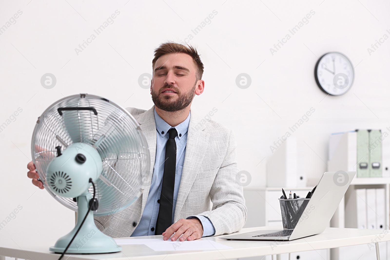 Photo of Man enjoying air flow from fan at workplace