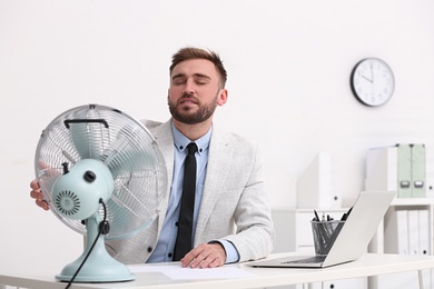 Man enjoying air flow from fan at workplace