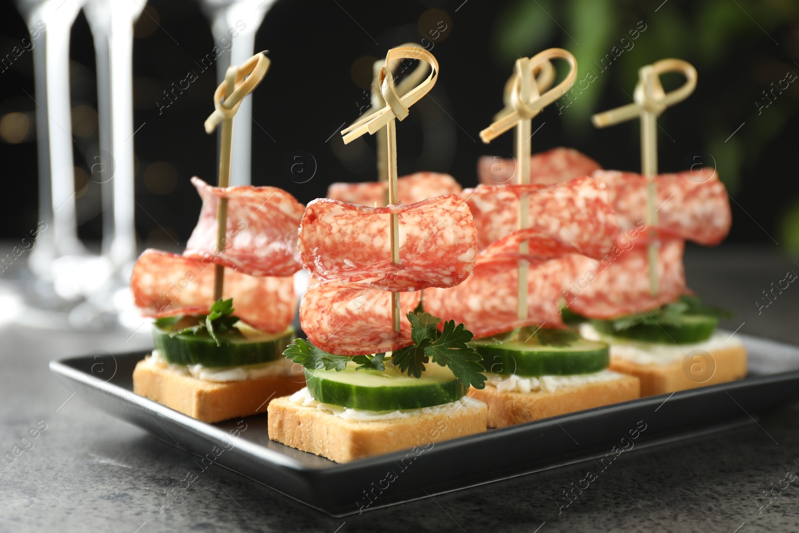 Photo of Tasty canapes with salami, cucumber and cream cheese on grey table, closeup