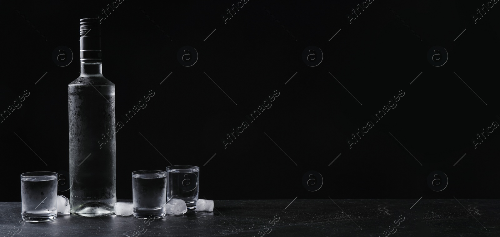 Image of Bottle of vodka and shot glasses with ice on table against black background, space for text. Banner design