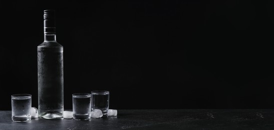 Bottle of vodka and shot glasses with ice on table against black background, space for text. Banner design