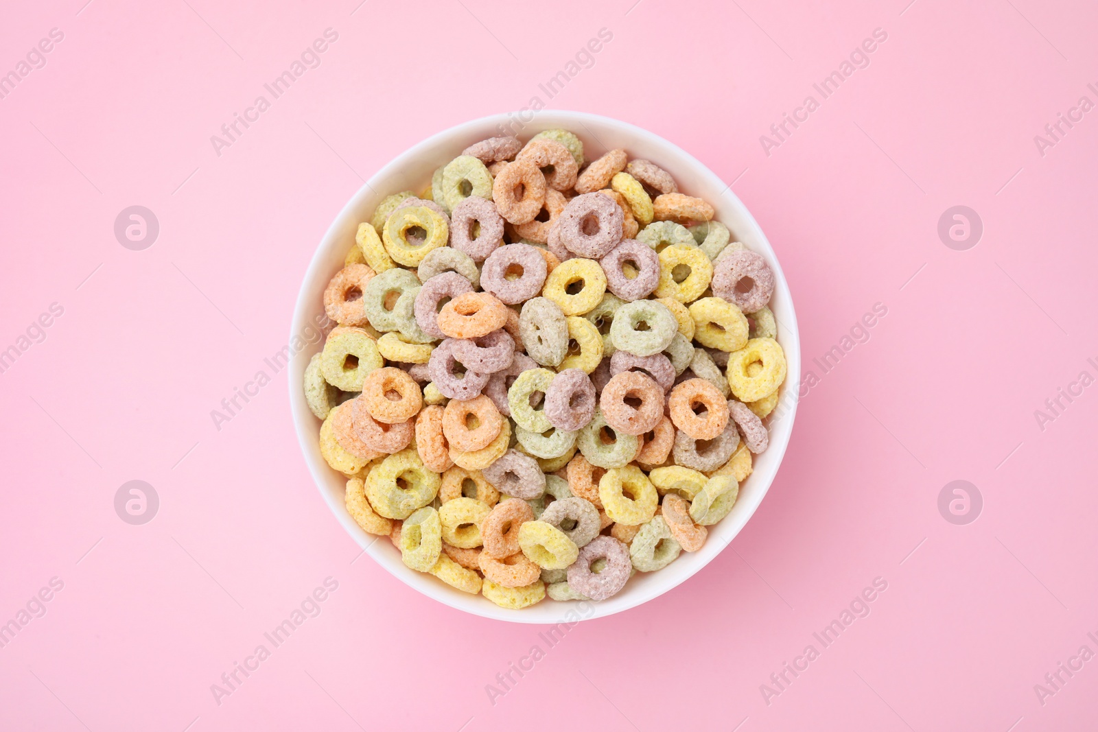 Photo of Tasty cereal rings in bowl on pink table, top view