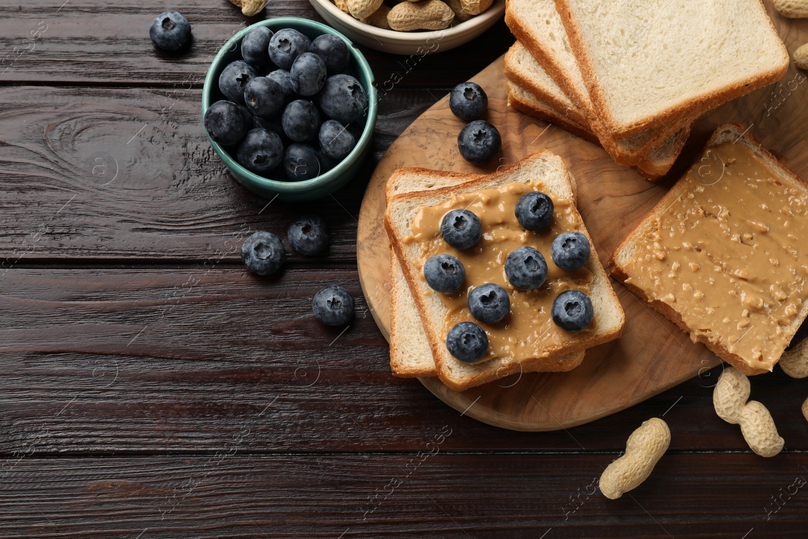 Photo of Delicious toasts with peanut butter, blueberries and nuts on wooden table, flat lay. Space for text