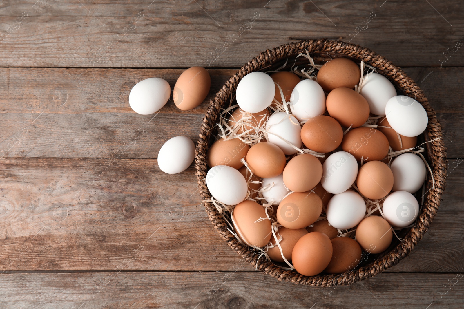 Photo of Basket with raw chicken eggs on wooden background, top view. Space for text