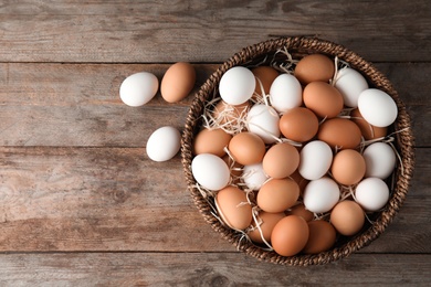 Photo of Basket with raw chicken eggs on wooden background, top view. Space for text