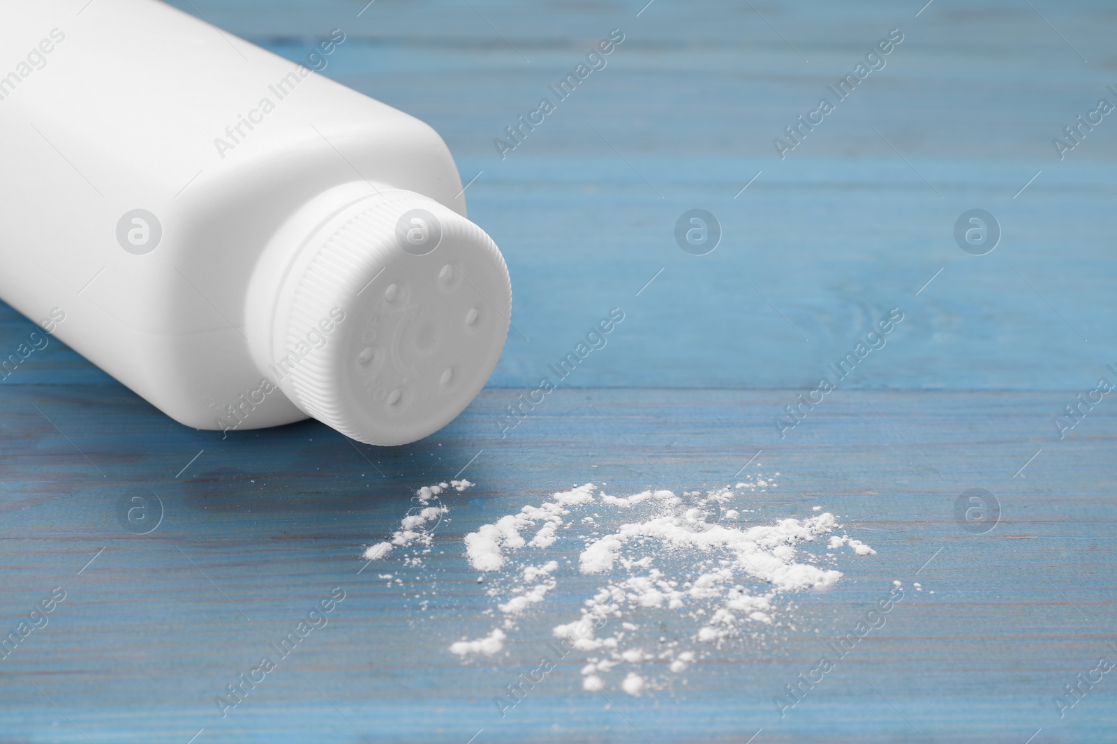 Photo of Bottle and scattered baby powder on light blue wooden table, closeup. Space for text