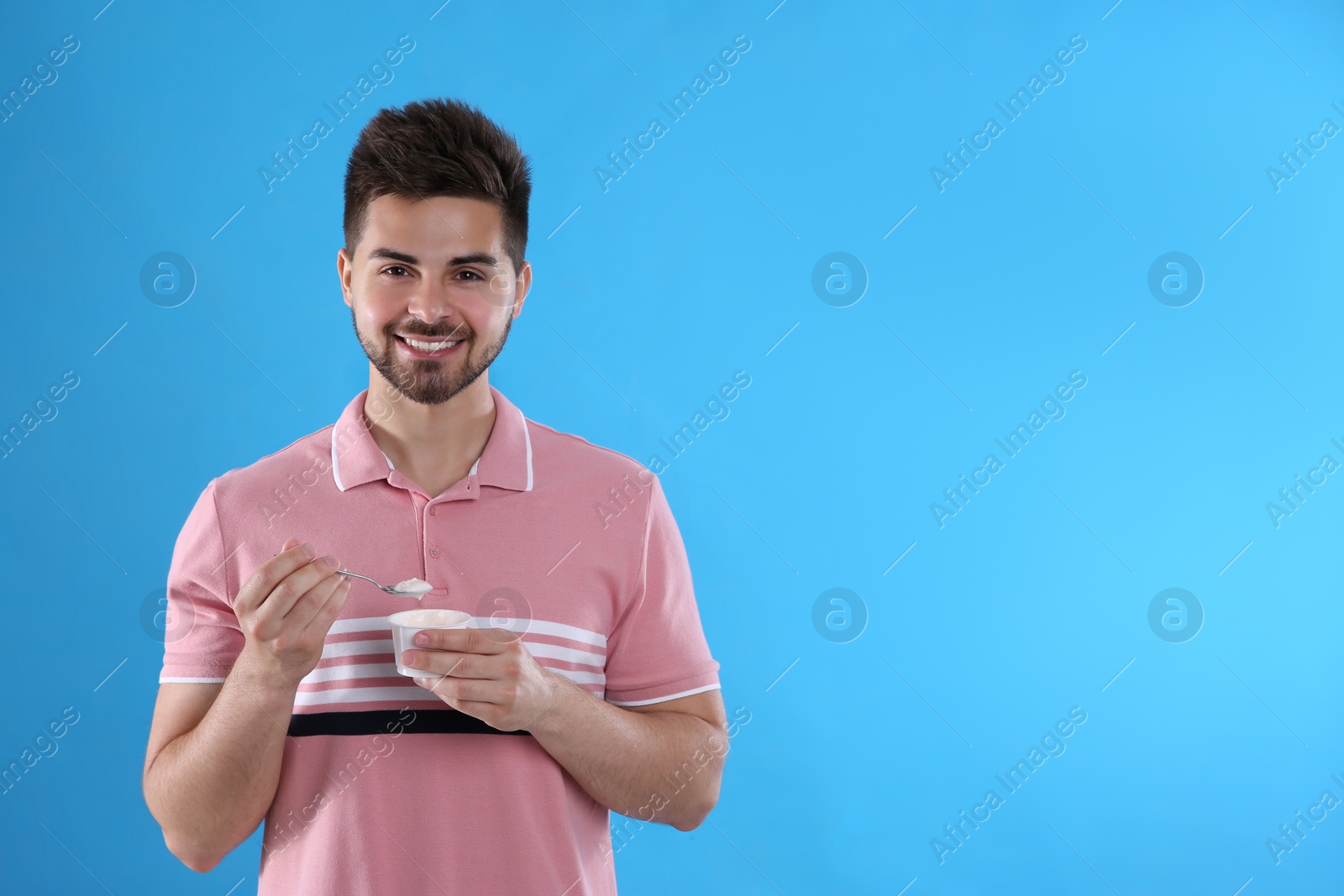 Photo of Happy young man with yogurt and spoon on light blue background. Space for text
