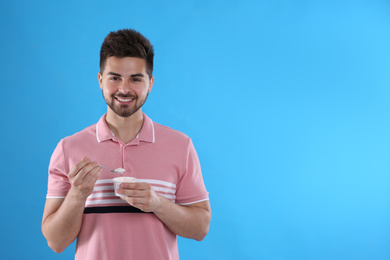 Happy young man with yogurt and spoon on light blue background. Space for text