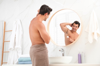 Photo of Handsome young man applying deodorant in bathroom