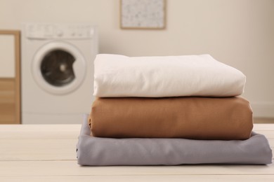 Photo of Stack of clean bed linens on white wooden table in laundry room