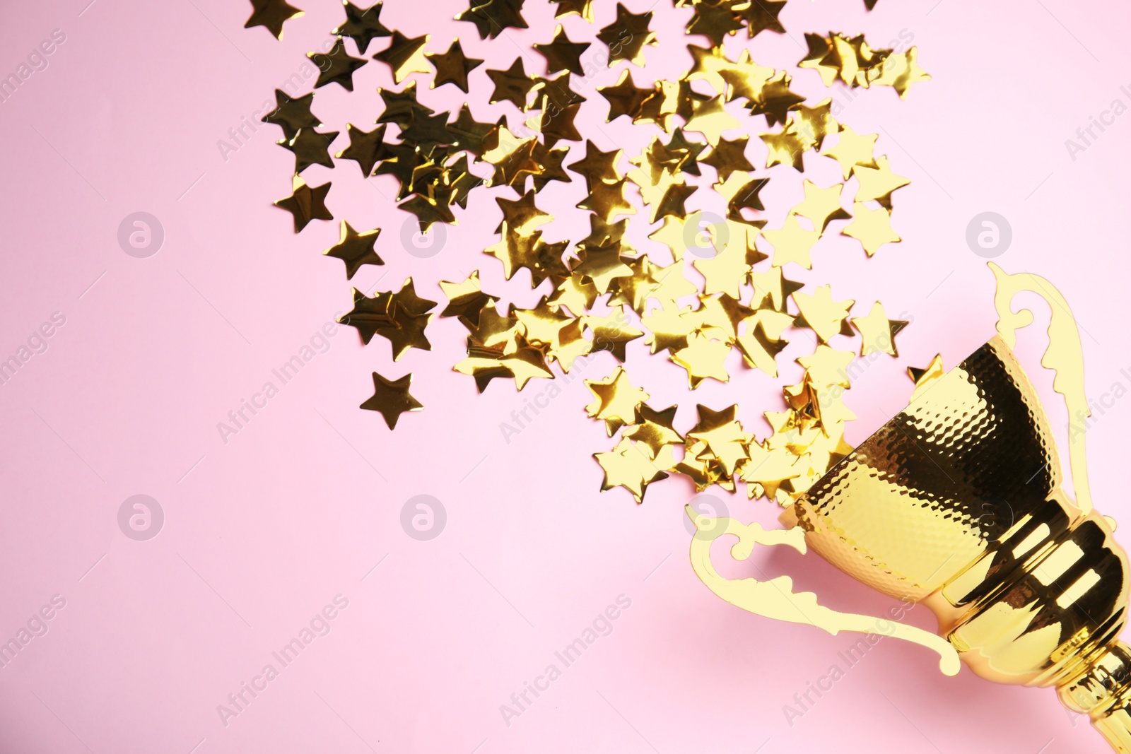 Photo of Golden trophy cup with confetti stars on pink background, flat lay