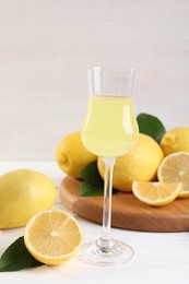 Photo of Liqueur glass with tasty limoncello, lemons and green leaves on white wooden table