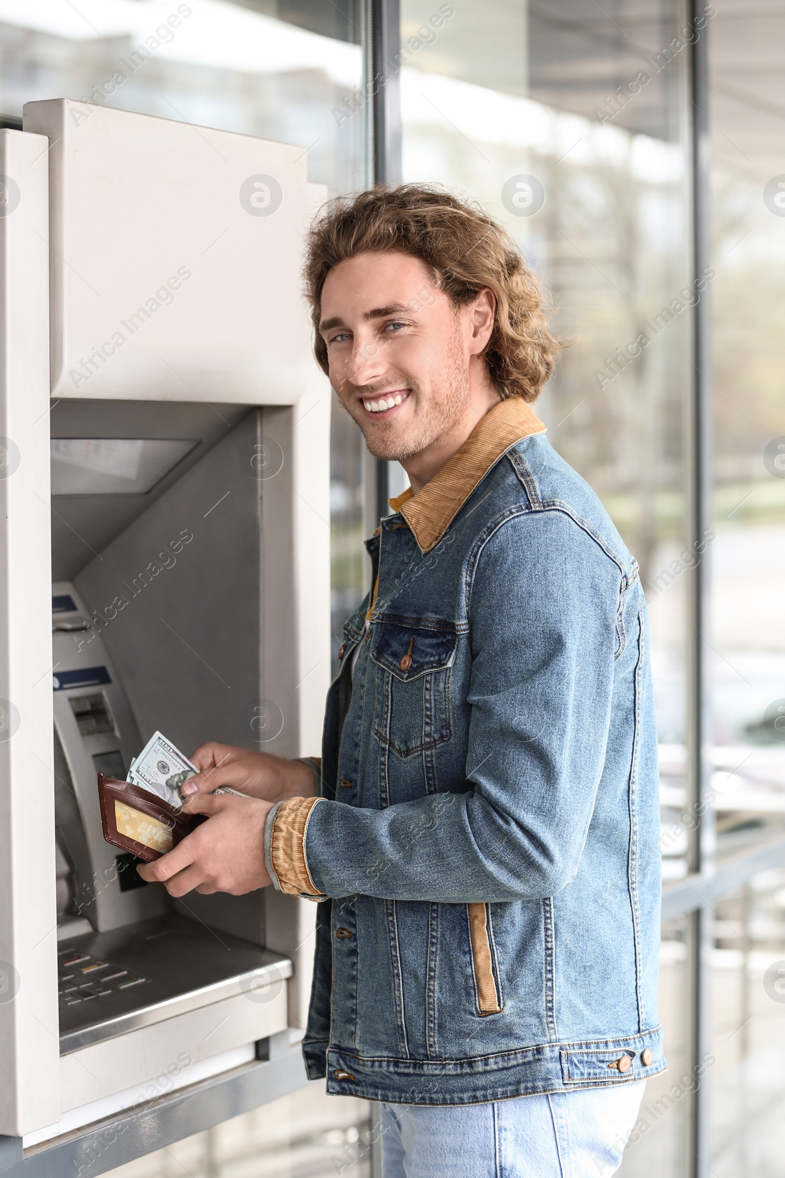 Photo of Young man with money near cash machine outdoors