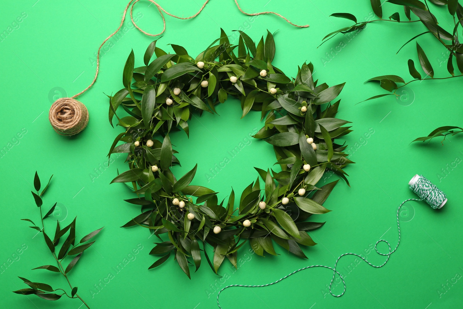 Photo of Beautiful handmade mistletoe wreath and florist supplies on green background, flat lay. Traditional Christmas decor