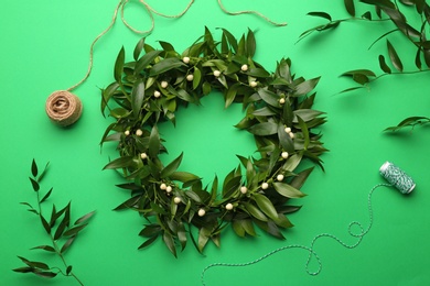 Photo of Beautiful handmade mistletoe wreath and florist supplies on green background, flat lay. Traditional Christmas decor