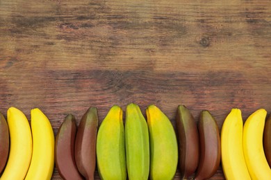 Many different bananas on wooden table, flat lay. Space for text