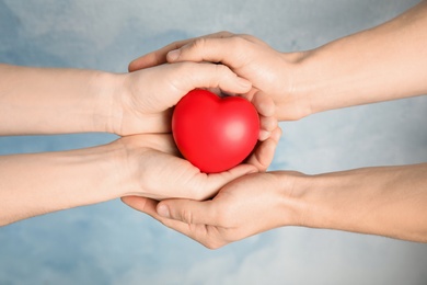 People holding red heart against color background, closeup. Cardiology concept