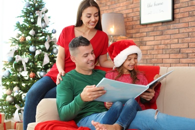 Happy parents and child reading fairy tales together at home on Christmas day