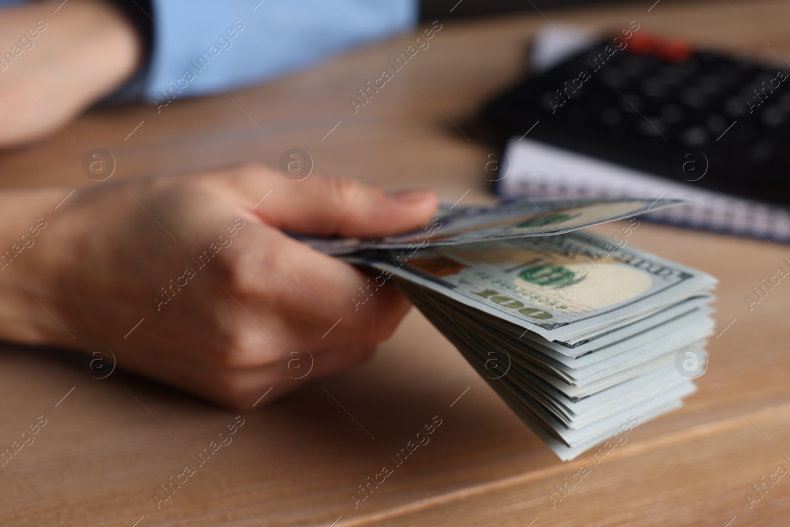 Photo of Money exchange. Woman holding dollar banknotes at wooden table, closeup