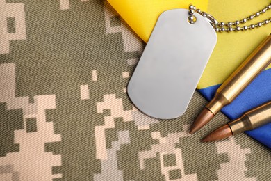 Photo of Military ID tag, bullets and Ukrainian flag on pixel camouflage, flat lay. Space for text