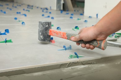 Photo of Worker with rubber hummer installing tiles indoors , closeup