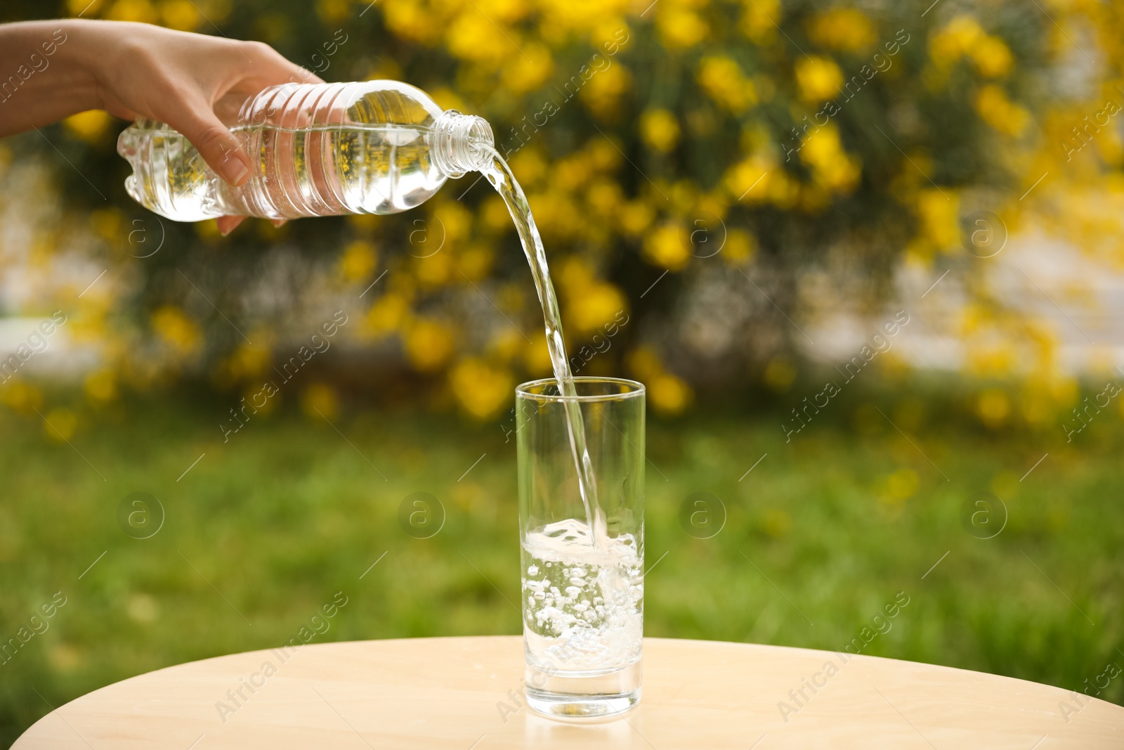 Photo of Woman pouring water from bottle into glass on table outdoors, closeup