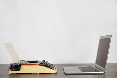 Old typewriter and laptop on table against light background, space for text. Concept of technology progress