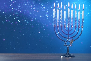 Image of Hanukkah celebration. Menorah with burning candles on wooden table against blue background, space for text