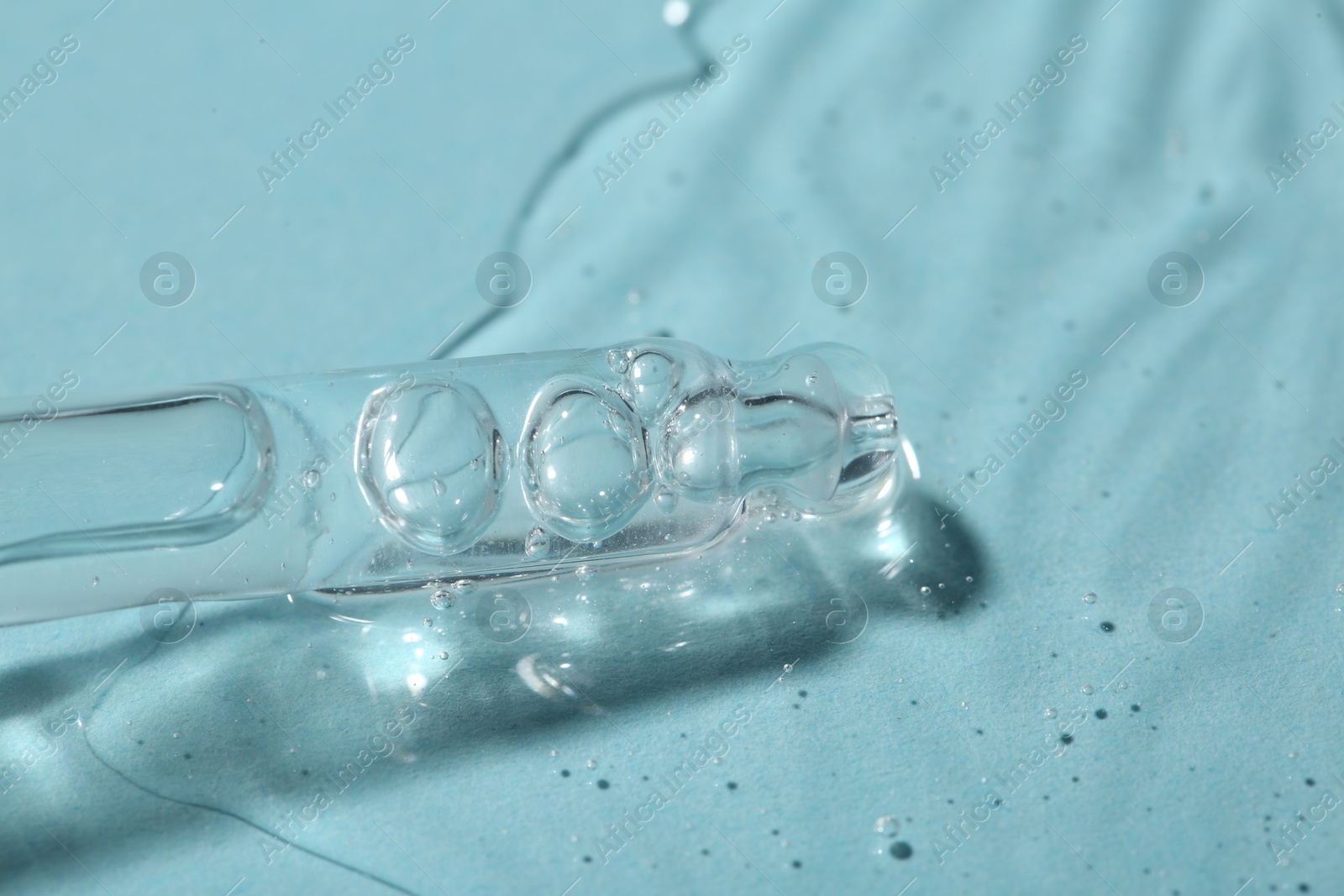 Photo of Dripping cosmetic serum from pipette onto light blue background, macro view