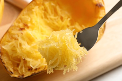 Fork with flesh of cooked spaghetti squash on blurred background, closeup