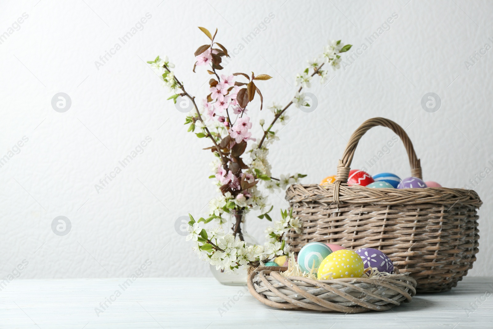 Photo of Composition with painted Easter eggs and blossoming branches on table. Space for text