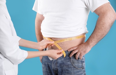Photo of Doctor measuring overweight man's waist on color background, closeup