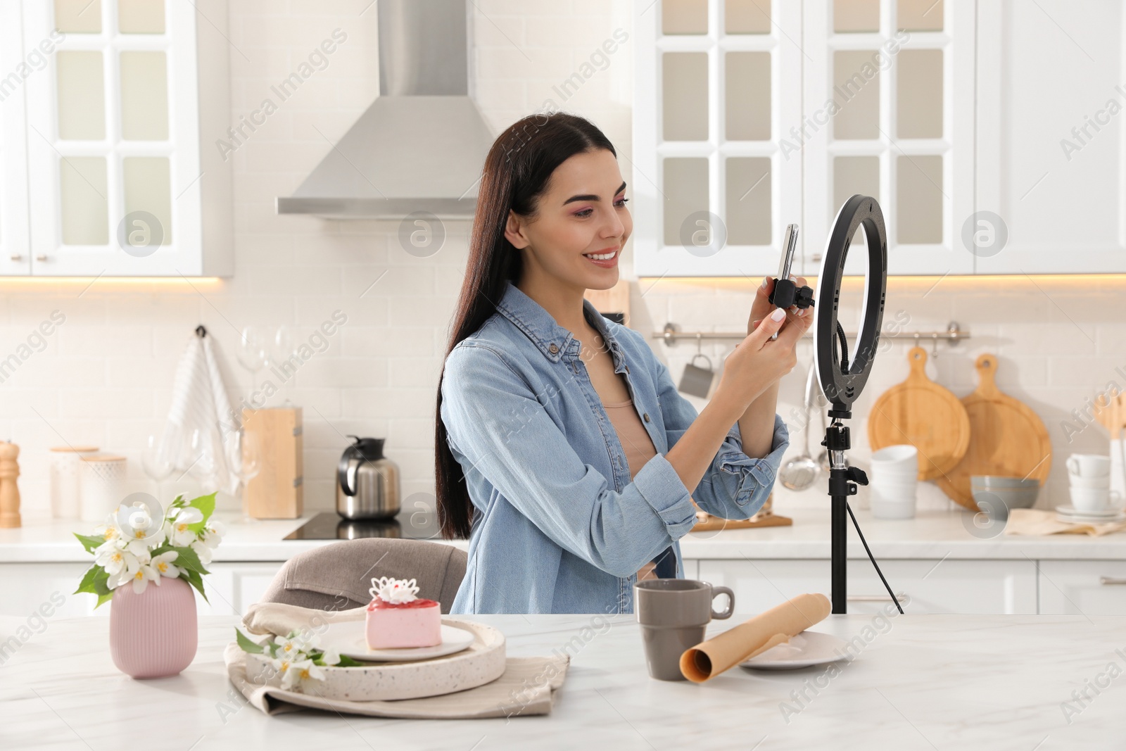 Photo of Blogger preparing for video recording in kitchen at home. Using smartphone and ring lamp