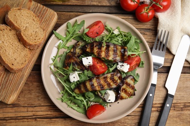 Photo of Delicious salad with roasted eggplant, feta cheese and arugula served on wooden table, flat lay