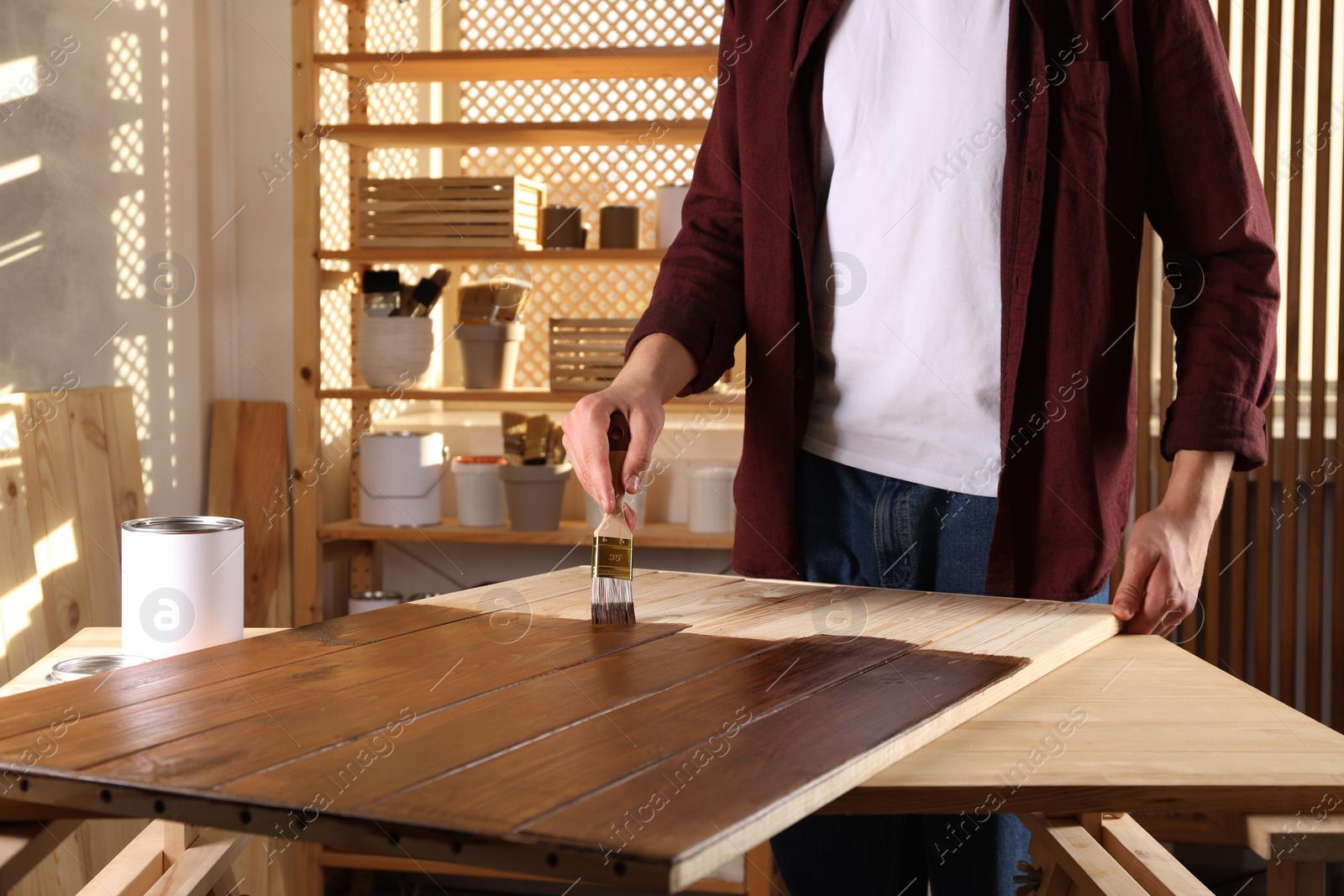 Photo of Man with brush applying wood stain onto wooden surface indoors, closeup