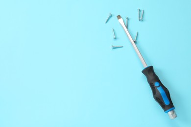 Photo of Screwdriver with black handle and screws on light blue background, flat lay. Space for text