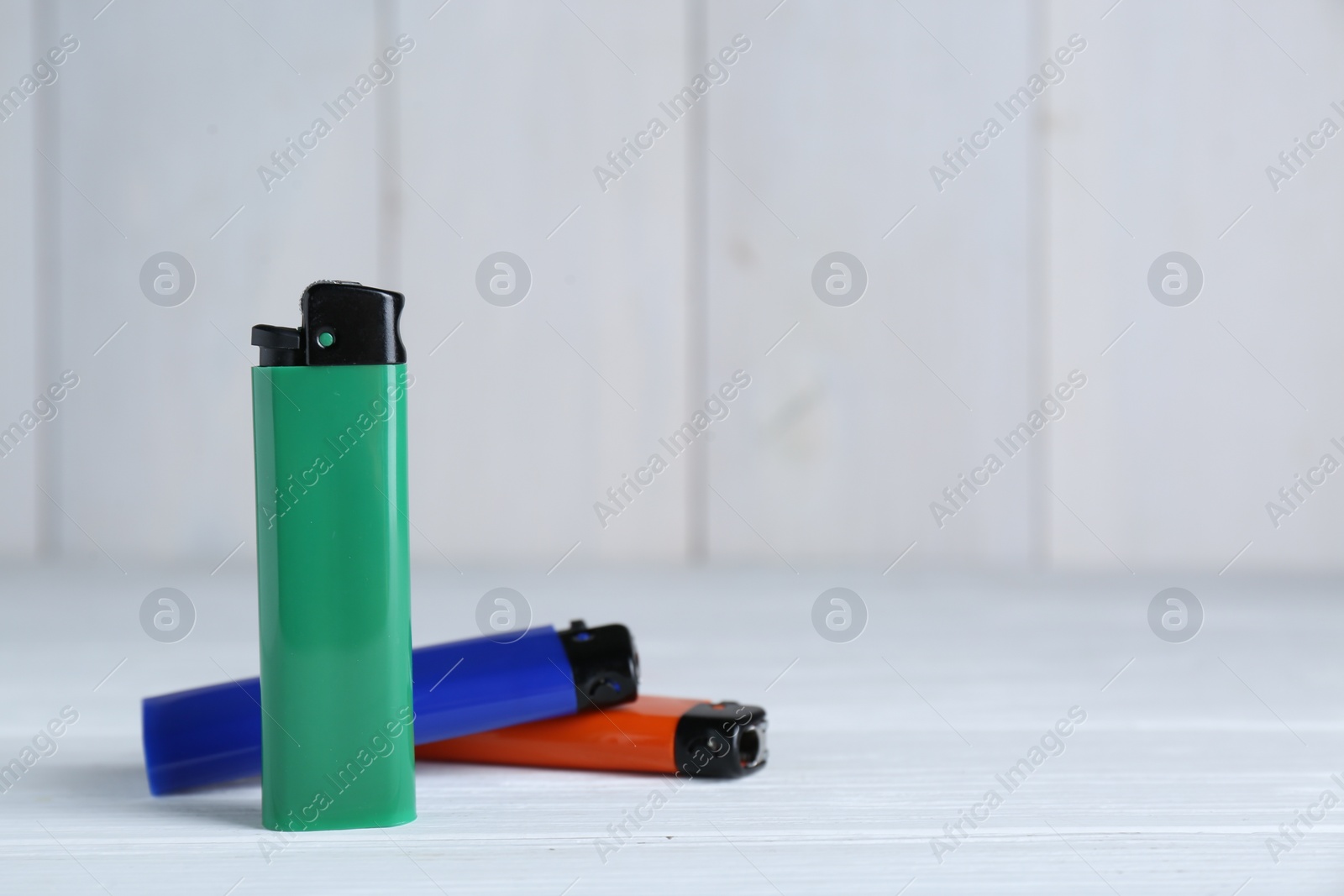 Photo of Stylish small pocket lighters on white wooden table, space for text