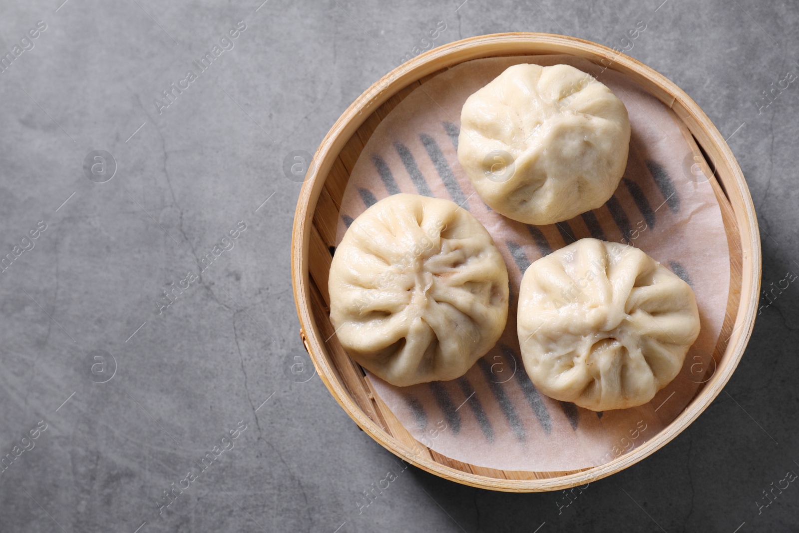 Photo of Delicious bao buns (baozi) on grey textured table, top view. Space for text