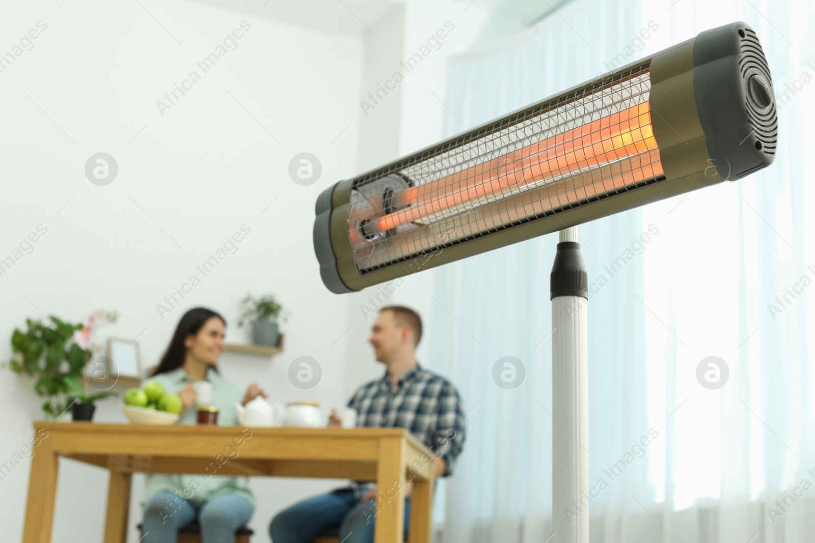 Photo of Couple spending time in room with modern electric infrared heater, focus on appliance