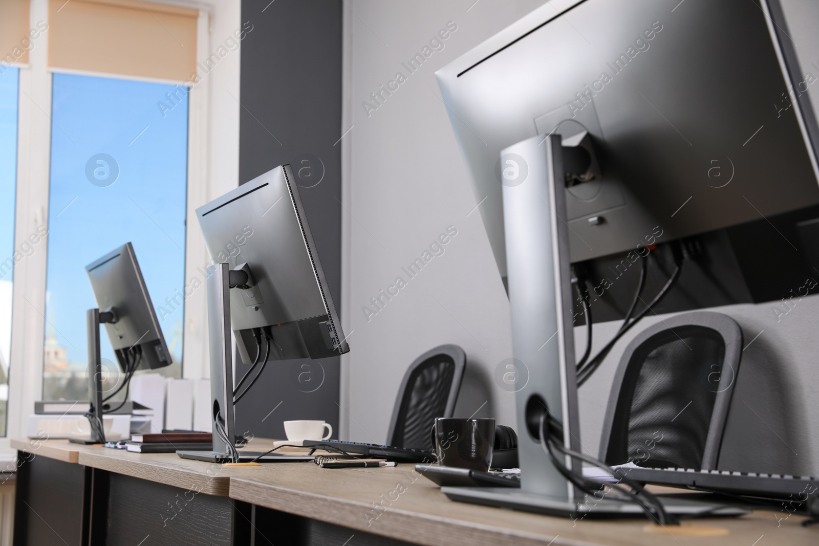 Photo of Open office interior. Modern workplaces with computers near light grey wall