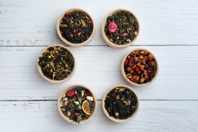 Different kinds of dry herbal tea in bowls on white wooden table, flat lay