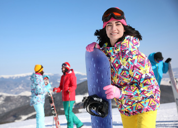 Photo of Young woman with snowboard at ski resort, space for text. Winter vacation