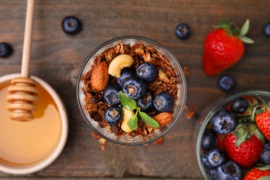 Photo of Tasty granola, berries, nuts and honey on wooden table, flat lay