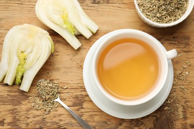 Fennel tea in cup, seeds and fresh vegetable on wooden table, flat lay