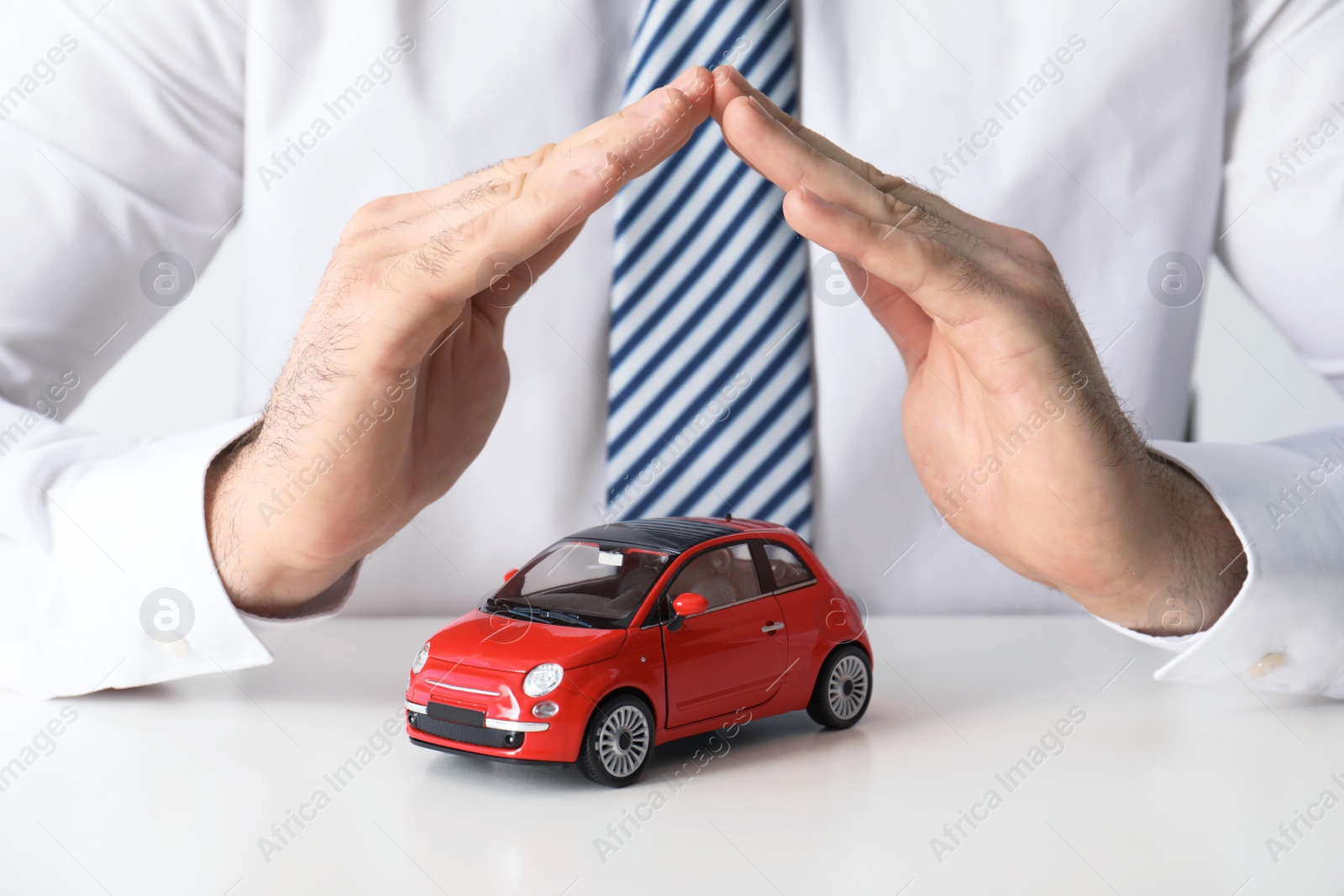 Photo of Male insurance agent covering toy car at table, closeup