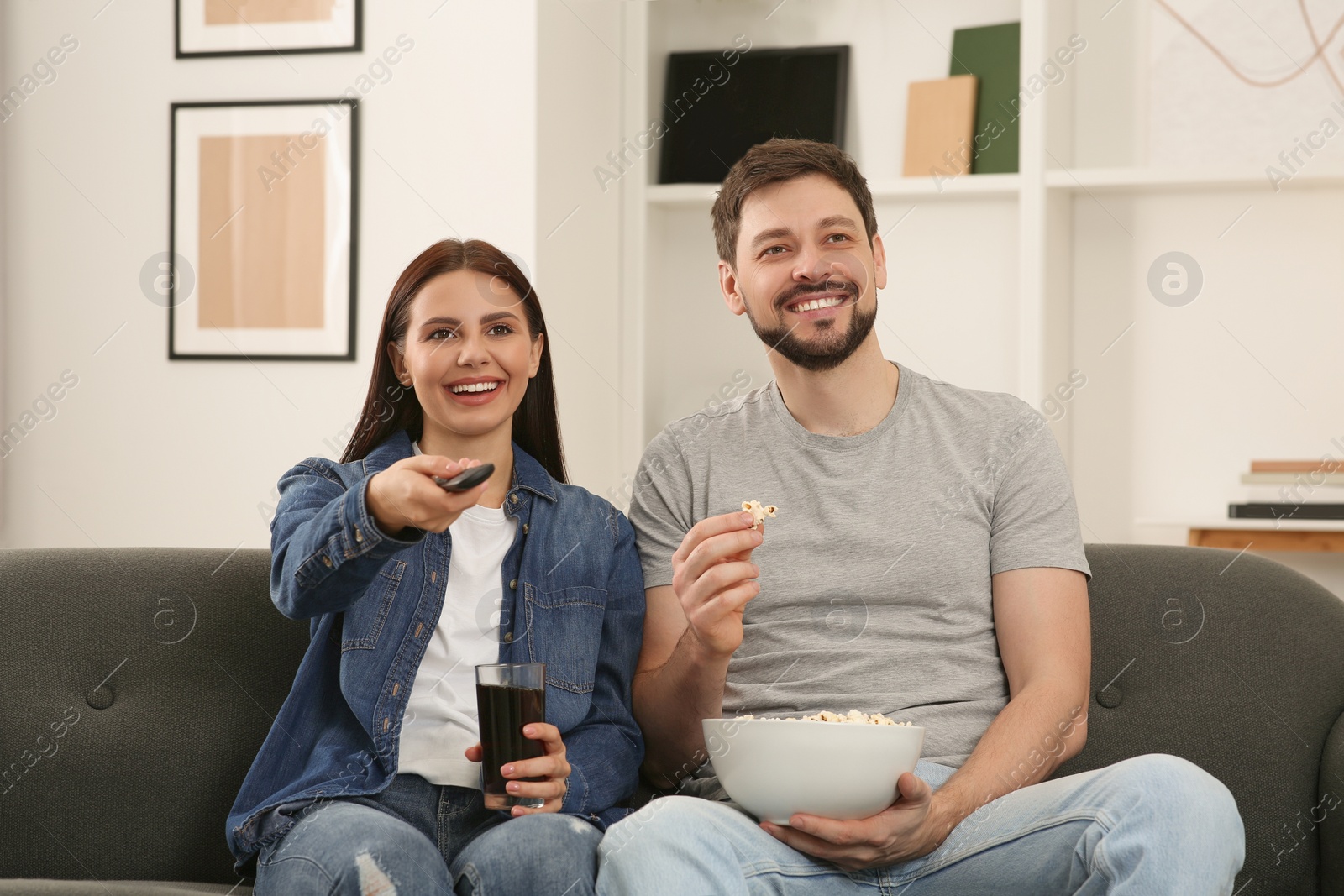 Photo of Happy couple watching show at home. Woman changing TV channels with remote control