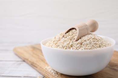 Raw barley groats and scoop in bowl on white wooden table, closeup. Space for text