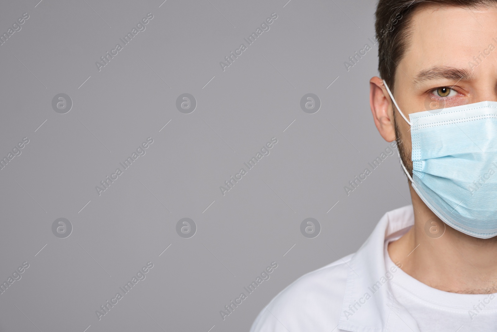 Photo of Doctor or medical assistant (male nurse) in uniform with protective mask on light grey background, closeup. Space for text