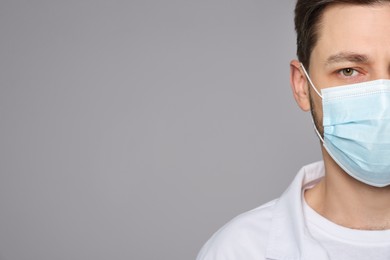 Doctor or medical assistant (male nurse) in uniform with protective mask on light grey background, closeup. Space for text